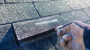 Close-up of curled and cracked asphalt shingles on a residential roof beside a handheld inspection tool.